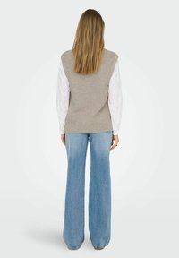 Top grigio a costine senza maniche abbinato a jeans blu in denim a gamba ampia; il top ha una finitura testurizzata e i jeans presentano un taglio tradizionale.