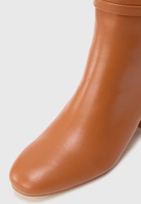 Botte chelsea couleur tan en cuir lisse. Présente une pointe effilée et un dessus courbé avec des coutures discrètes. Pas de matériel ou de motifs visibles.