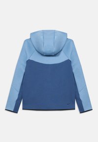 Mikina s kapucňou so rozdeleným dizajnom v svetlom a tmavom modrom, so hladkým povrchom a kontrastným čiernym lemovaním. Logo Nike v pravom dolnom rohu.