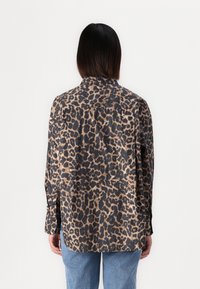 Leopard print shirt in black, brown, and tan colors, featuring a collar, button-up front, and long sleeves with slightly tapered cuffs.