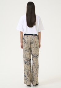 Beige pants with a blue marbled pattern, wide-leg design, and elastic waistband, paired with a white short-sleeve top.