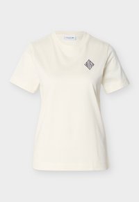 Μπεζ βαμβακερό T-shirt με στρογγυλή λαιμόκοψη, κοντά μανίκια και κέντημα με λογότυπο σε σχήμα ρόμβου στο αριστερό στήθος. Λεία υφή.