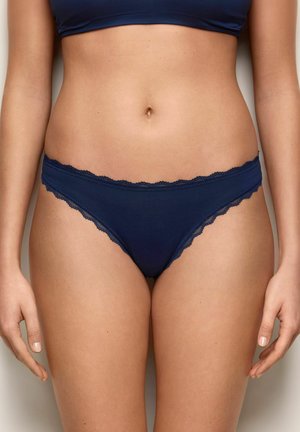 Frau trägt marineblaue Bikini-Unterwäsche mit Spitzenbesatz und einen passenden Sport-BH, zu sehen vom mittleren Torso bis zu den oberen Oberschenkeln.