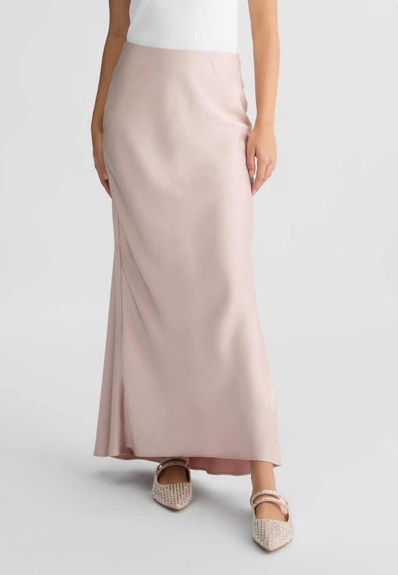 Maxi gonna in satin rosa pallido con una texture liscia, caratterizzata da una silhouette dritta e un discreto spacco laterale. Abbinata a delle ballerine decorate.