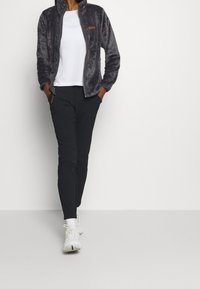 Grå fleecjacka med hög krage, dragkedjestängning och sidofickor, kombinerad med svarta byxor och vita sneakers. Slät textur, avslappnad stil.