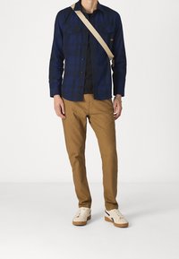 Marinblå och blå rutigt långärmad skjorta över en svart t-shirt, ihop med beige slim fit byxor och beige sneakers med svarta accenter.