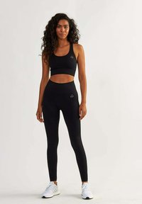 Black sports bra and high-waisted leggings made of stretchy fabric, featuring a subtle logo on both pieces, worn with white athletic shoes.