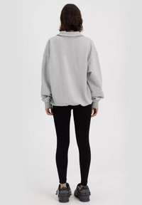 Szary, oversize'owy sweatshirt z kołnierzem, długimi rękawami i ściągaczami, w zestawie z czarnymi leginsami i szarymi trampkami. Prosty design, luźny krój.