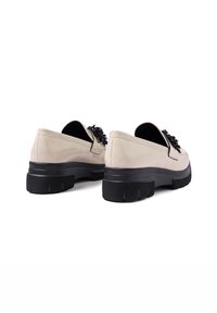 Scarpe slip-on beige con una superficie testurizzata, caratterizzate da un accento decorativo nero e una suola nera spessa e chunky.