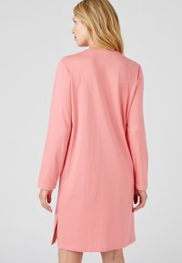 Abito lungo rosa a maniche lunghe realizzato in tessuto morbido, con scollatura rotonda, fessure laterali e dettagli decorativi sui polsini.