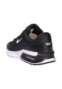 Zapatilla deportiva negra con parte superior de malla texturizada y talón de goma suave. Presenta acentos en blanco y una unidad de amortiguación de aire visible.