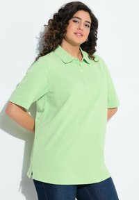 Světle zelené polo tričko s límečkem, krátkými rukávy a tříknopkovým rozparkem; má boční rozparky na spodním lemu pro snadnější pohyb.