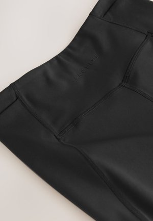 Gros plan sur un legging de sport noir avec une taille haute et des coutures visibles, avec un logo subtil « ACTIVE » sur le tissu.