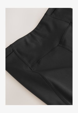 Közeli kép fekete sportos leggingsről, magas derékrésszel és látható varrásokkal, a textilen diszkrét "ACTIVE" logóval.