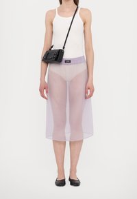 Läpinäkyvä lavendeli midi-hame, jossa on joustava vyötärö, yhdistetty valkoiseen toppiin ja pieneen mustaan olkalaukkuun. Mustat ballerinat jalassa.