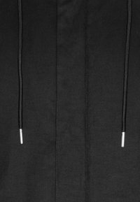 Tissu noir avec deux cordons noirs suspendus verticalement, chacun se terminant par des embouts métalliques argentés.