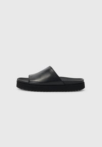 Sorte skinnsandaler i svart har en glatt overdel med en lav, tykk gummisåle og en teksturert kant for bedre grep.
