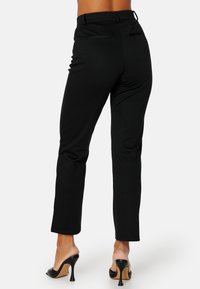 Černé kalhoty s vysokým pasem vyrobené z elastického materiálu, s hladkou texturou, úzkým střihem a zadními kapsami.