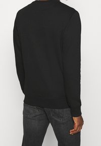 Sudadera negra con cuello redondo, mangas largas y puños y dobladillo acanalados. Textura suave, sin patrones visibles ni detalles metálicos.