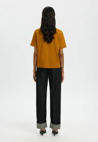 Sinepju dzeltenas īsām piedurknēm topiņš, brīvs piegriezums; kopā ar melnajām platām biksēm ar saliektu apakšējo malu kontrastējošā pelēkā krāsā.