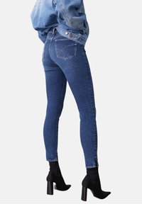 Kapeat siniset farkut korkealla vyötäröllä, joissa on kaksi takataskua ja sivusaumavetoketjut. Yhdistettynä mustiin korkokenkiin ankle-bootsi.