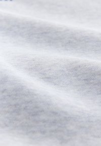 Material din țesătură gri deschis, cu textură fină tricotată și pliuri subtile care creează umbre delicate.