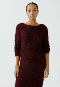 Bordeauxfarbendes Strickkleid mit einer weichen, flauschigen Textur, weitem Ausschnitt und dreiviertellangen Ärmeln, das einen lockeren, entspannten Schnitt aufweist.