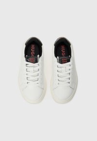 Et par hvite lave sneakers med svarte tunger, røde merkevarer, hvite lisser og svart innvendig fôr på en ensfarget bakgrunn.