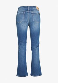 Jeans de mezclilla azul acampanados con una cintura de altura media, dos bolsillos traseros con costuras decorativas y una etiqueta de marca de cuero marrón en la cinturilla.