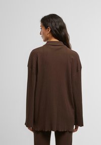 Brun ribbet oversized skjorte med krave; har en rå kant og lange ærmer, der fremhæver et struktureret stof og en afslappet pasform.
