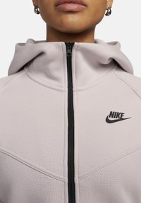 Lichtroze zip-up hoodie met een zwarte rits en Nike-logo, voorzien van een capuchon en gestructureerde stof met naaddetails.