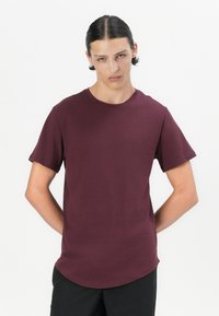 Camiseta de manga corta burdeos en una tela suave y lisa. Cuenta con un escote redondo y un dobladillo ligeramente curvado. Diseño simple y elegante.