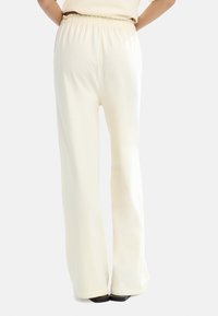 Jasne kremowe spodnie o szerokich nogawkach, wykonane z gładkiego, elastycznego materiału. Posiadają elastyczną talię i rozkloszowany dół, co zapewnia swobodny krój.