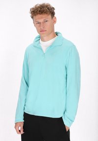 Lichtblauwe fleece pullover met een halve rits, lange mouwen en een rechte zoom. De stof lijkt zacht en glad, met een eenvoudig ontwerp.