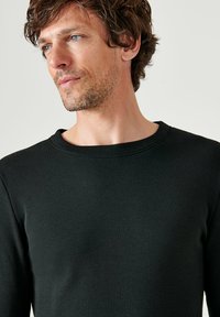 Maglietta nera a maniche lunghe e scollo rotondo, con una silhouette aderente, realizzata in un tessuto liscio. Design minimalista con collo e polsini a coste.