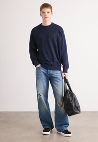 Tengerész navy crewneck pulóver, világoskék szakadt farmernadrág, fekete magas szárú tornacipő és fekete bőrtáska cipzárral és rövid füllel.