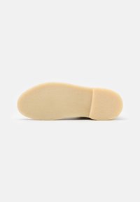 Suela de zapato hecha de goma de color beige claro con una superficie lisa y ligeramente texturizada y forma de punta redondeada. Diseño plano sin patrones o acentos visibles.