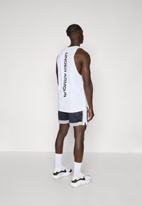 Hvit ermeløs tank topp med "UNDER ARMOUR"-tekst på baksiden, sammen med mørke shorts med mesh tekstur og side slisser.