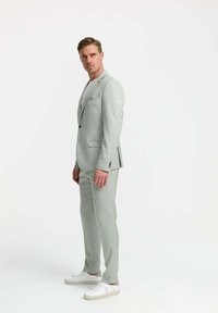 Hellgrauer maßgeschneiderter Anzug mit schlanker Passform, Revers und Seitentaschen, kombiniert mit weißen Sneakers für einen modernen Look.