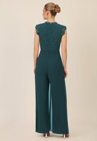 Teal jumpsuit met een kanten lijfje en scalloped halslijn, met wijde broekspijpen en zijsplitten. Glad materiaal met een getailleerde taille en een rits aan de achterkant.
