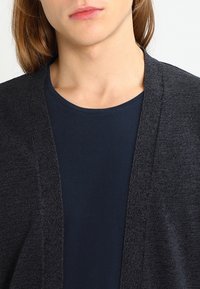 Ciemnoszary kardigan z otwartym przodem wykonany z teksturowanego materiału, noszony na jednolitym granatowym t-shircie, prezentujący casualowy design i luźne dopasowanie.