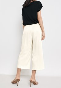 Zwarte korte-mouwen top gecombineerd met crèmekleurige wijd uitlopende broeken en nude hoge hakken. De broeken hebben plooien en een zachte textuur.