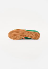 Grønn sneakers med et teksturert stoffoverdel, oransje aksent og en gummisåle med et sikksakkmønster for grep.