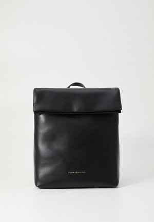 Svart lærryggsekk med fold-over topp, glatt tekstur og subtil gullmerke nederst. Minimalistisk design, rektangulær form.