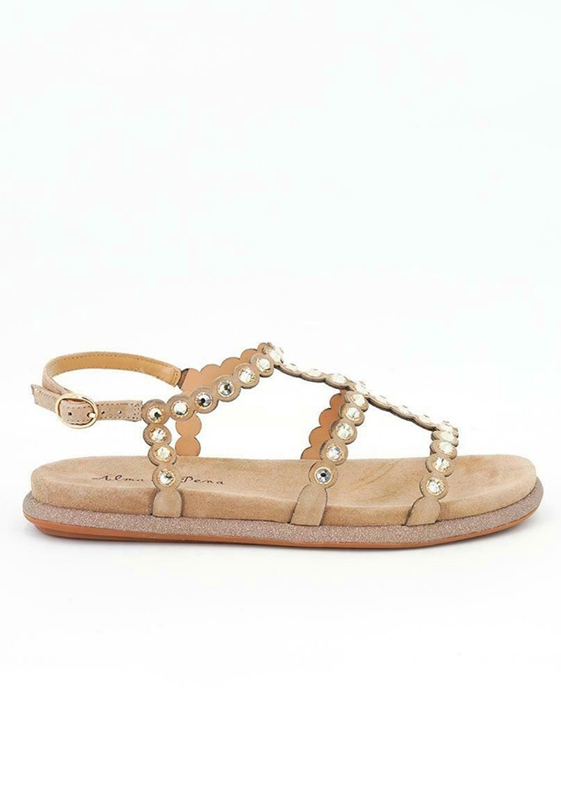 Beige mockask sandal med vågiga remmar, prydd med klara rhinestones. Har en justerbar vristrem och en platt, texturerad sula.
