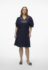 Vestido azul marino con mangas cortas y volantes, y un escote en V. Presenta bordados florales en colores vibrantes alrededor del escote.