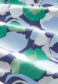 Tissu avec un motif abstrait coloré dans des nuances de vert, bleu, blanc et marine, présenté avec des plis naturels et une texture douce.