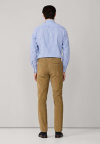 Lichtblauw en wit gestreept shirt met lange mouwen, en tan corduroy broek met achterzakken, van achteraf gezien. Blauwe suède schoenen.