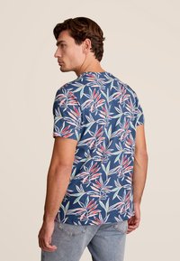 Marineblauw T-shirt met korte mouwen, versierd met een levendig bloemenpatroon in rood, groen en wit. De stof oogt zacht en lichtgewicht.