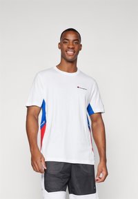 Camiseta de algodón blanca con acentos azules y rojos a los lados. Presenta un pequeño logo de Champion en el pecho. Mangas cortas, corte regular.